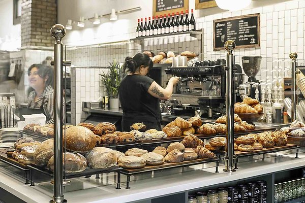 5 - Two baristas working and smiling behind a glass partion with bakery items and pastries at a bakery 5 - Two baristas working and smiling behind a glass partion with bakery items and pastries at a bakery